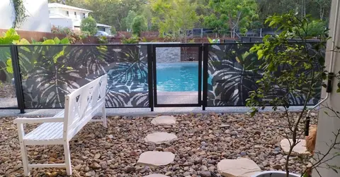 A run of black Monstera design panels with a white bench and pebble garden in front