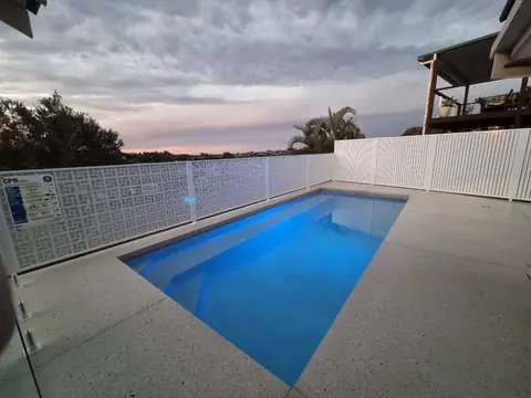 A Pearl White Nahosh design pool fence along a pool, with a white picket fence behind