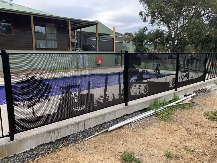 A black PoolPerf pool fence with a windmill, cows and trees cut into the panels, on a Victorian farm