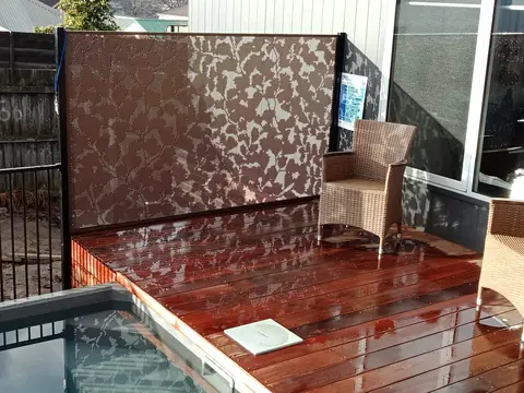 A rust coloured Ginko leaf screen behind a timber deck and spa in Queensland