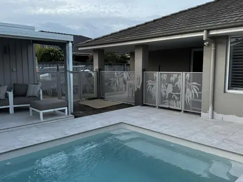 Light coloured panels with a kookaburra on a gum branch, between the columns of a home beside a pool