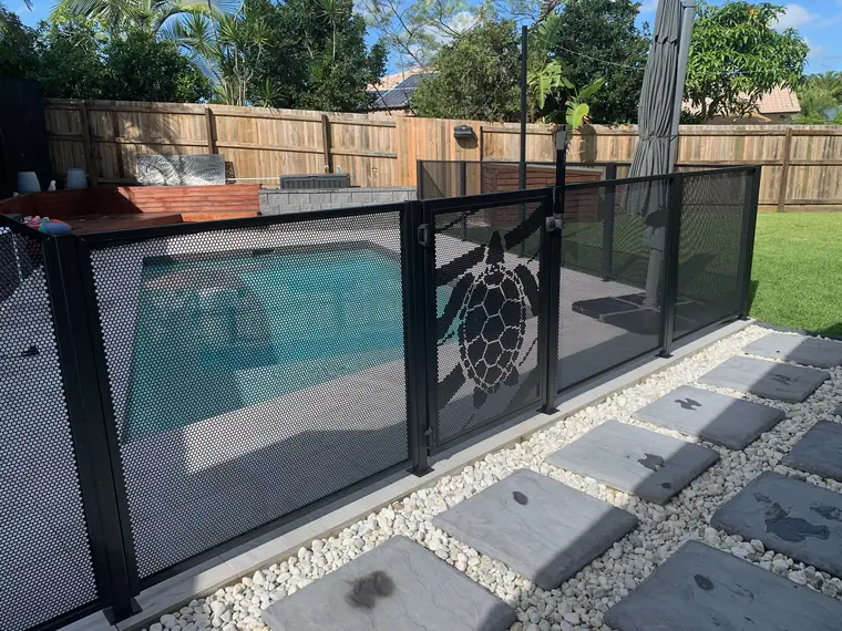 A black PoolPerf pool fence with sea turtles cut into the panels, beside a Queensland pool