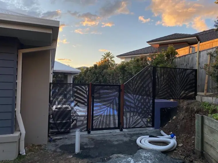 A black Palmy design gate and side fence beside a house at sunset