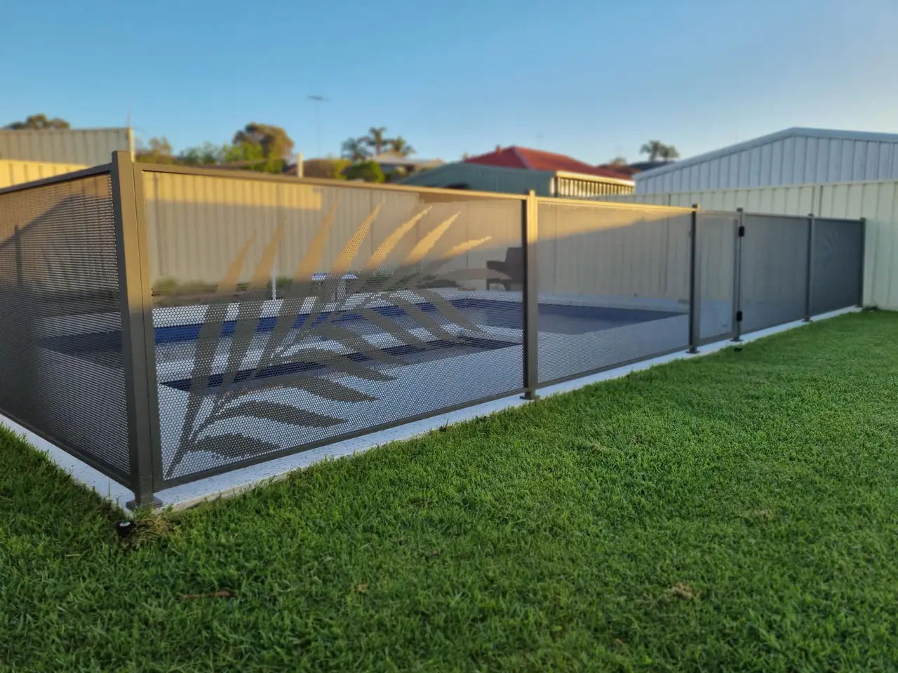 A single palm frond cut into a Woodland Grey PoolPerf panel beside a pool in Western Australia