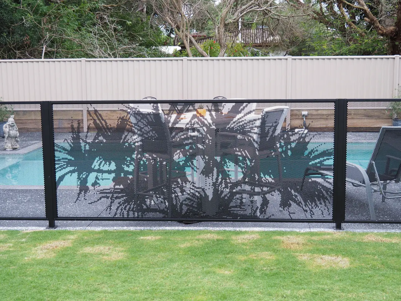 Black Pandanus design panels along a Queensland pool, with a colourbond fence and garden behind