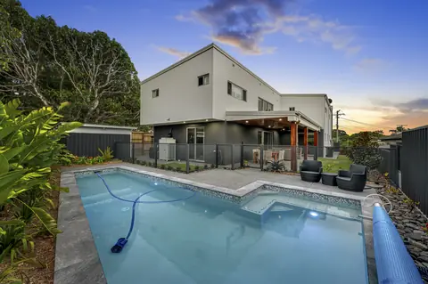 A Monument grey PurePerf fence around a pool and spa in front of a two storey Queensland home at dusk
