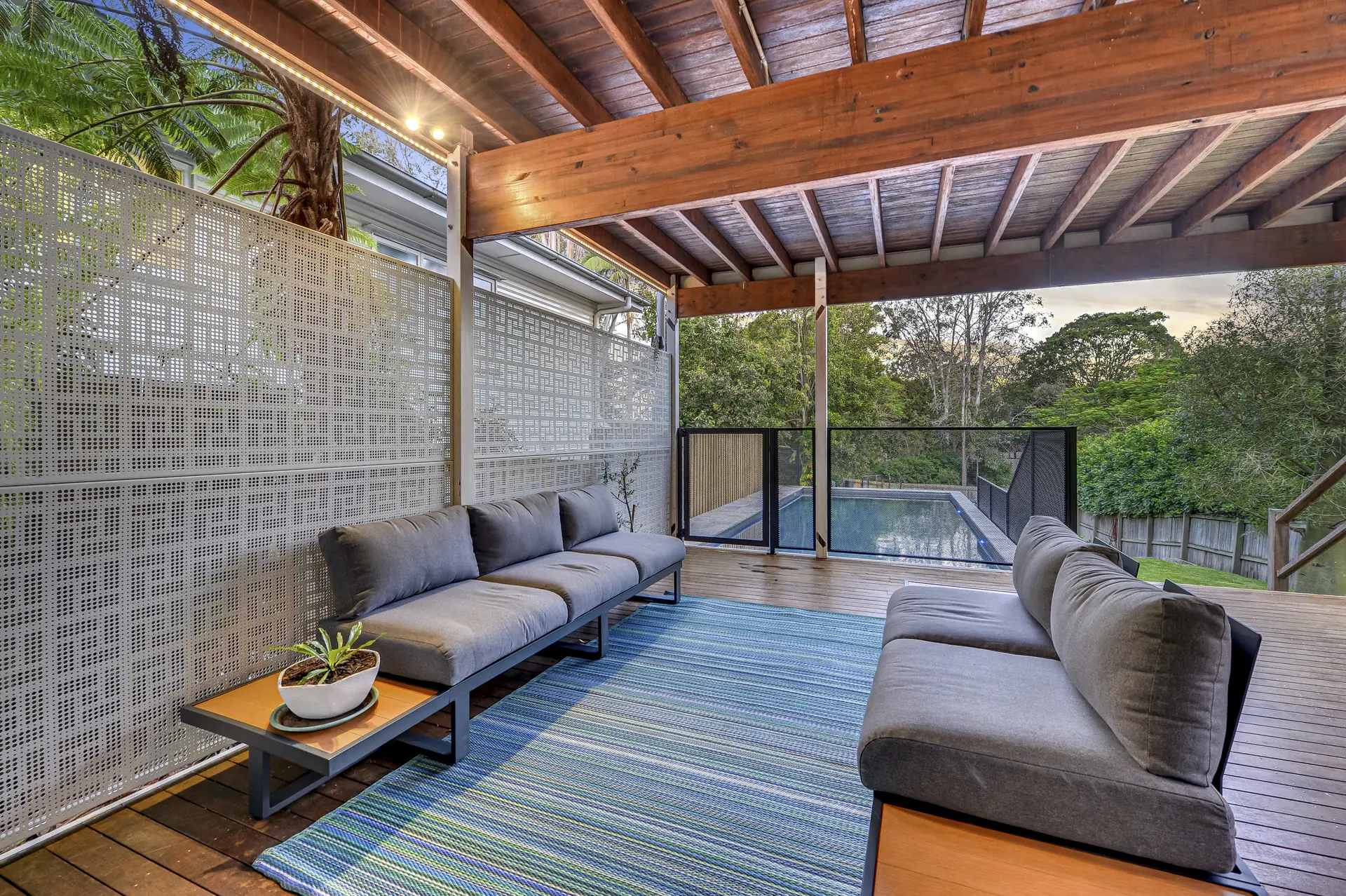 Nahosh design panels lining a covered deck with lounges, the pool and the treetops beyond