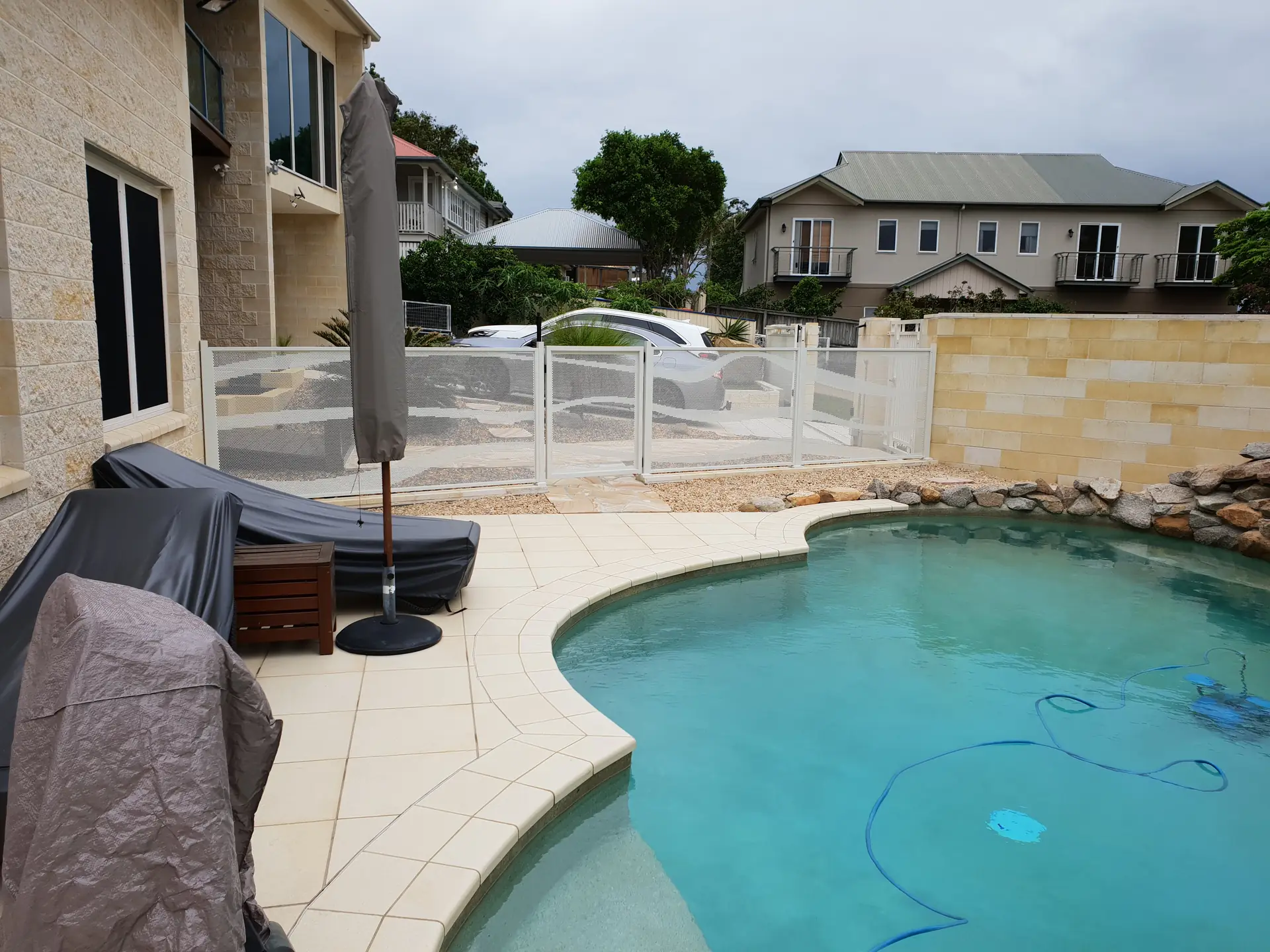 A silver Wave design PoolPerf fence around a curved pool in front of a two storey Queensland home