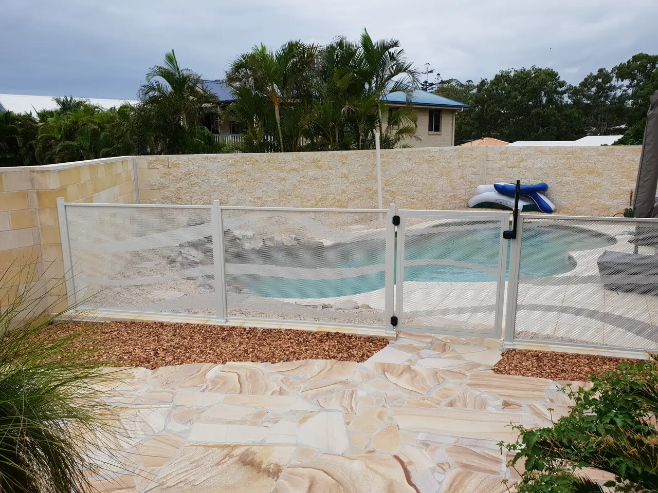 A silver Wave design pool fence and gate around a curved pool with sandstone paving