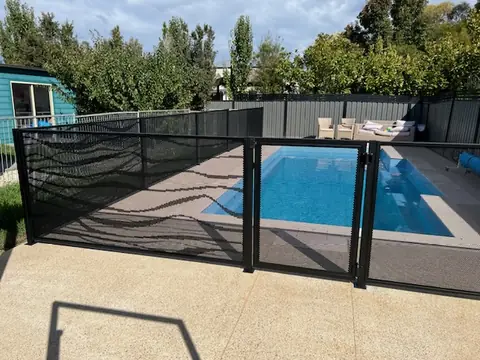 A black Wave design pool fence beside a timber cabin, with a long rectangular pool