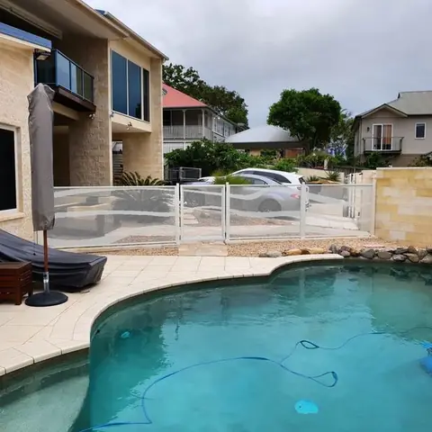A white Wave design pool fence beside a curved pool and a sandstone wall