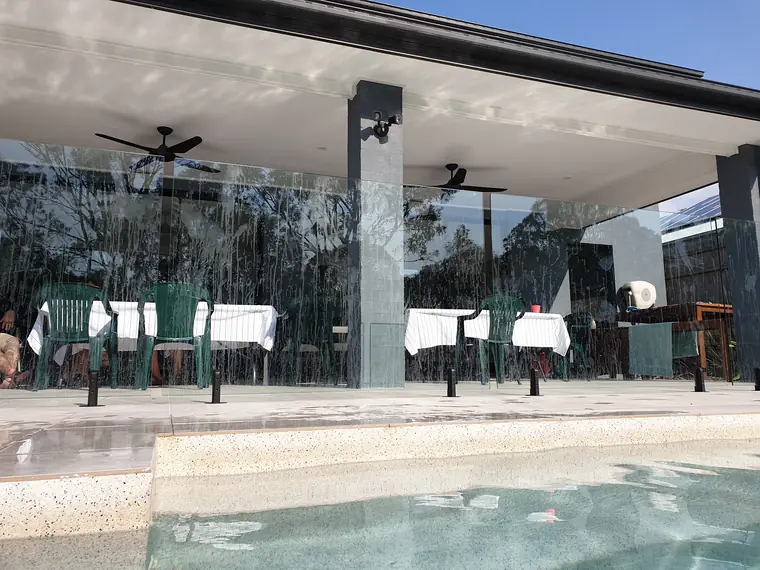 Glass pool fence panels streaked with water after a swim, in front of an outdoor dining area