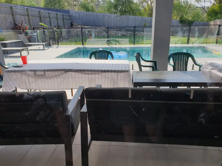 Looking out through a streaked, water-marked glass pool fence at an outdoor table and chairs