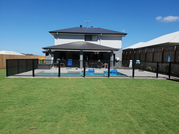 The whole job from the lawn: the house, the pool, a black PoolPerf fence along the front and the glass fence behind it