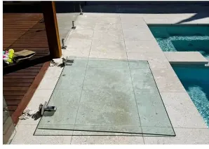 A glass pool fence panel blown flat onto the paving next to the pool after a wind storm