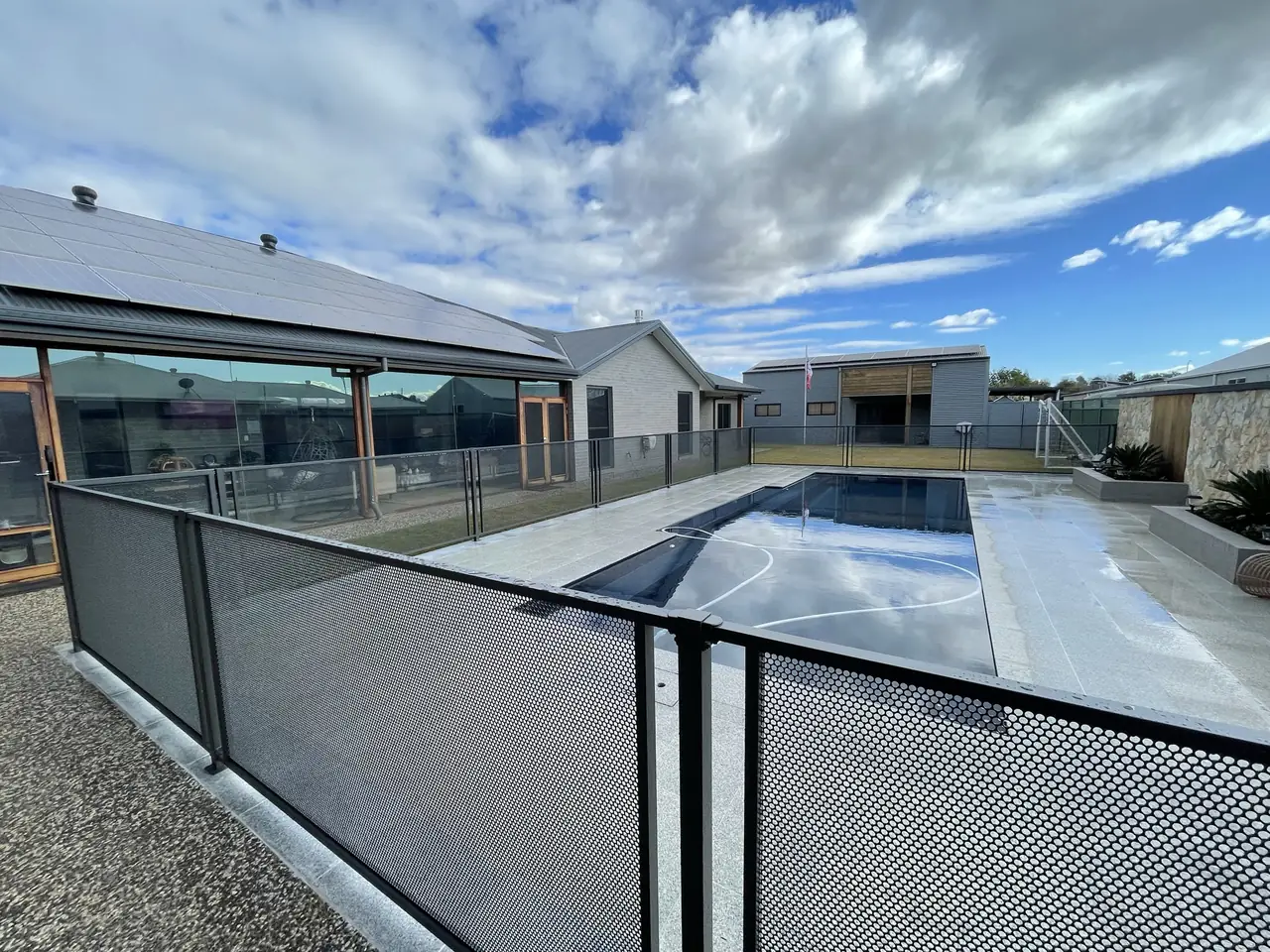 A modern grey home in New South Wales under a dramatic sky, with a Monument PoolPerf fence around the pool and the whole yard visible through it