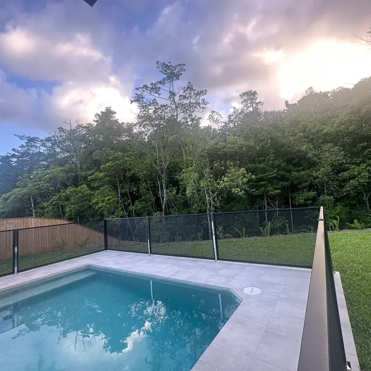 A pool under a cloudy sky with a black PoolPerf fence and bushland behind it