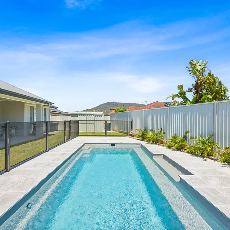A long lap pool beside a house in New South Wales with a black PoolPerf fence running along it