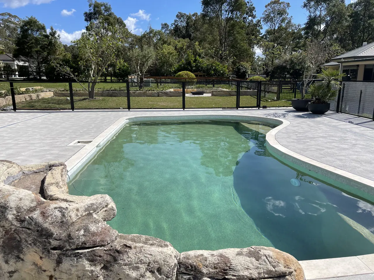 A wide lawn and a curved pool in New South Wales, with a black PoolPerf PurePerf fence you can see straight through