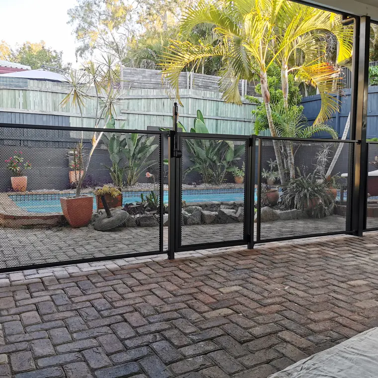 A PoolPerf gate and fence in a brick courtyard, with the pot plants and an outdoor bath clearly visible through the panel