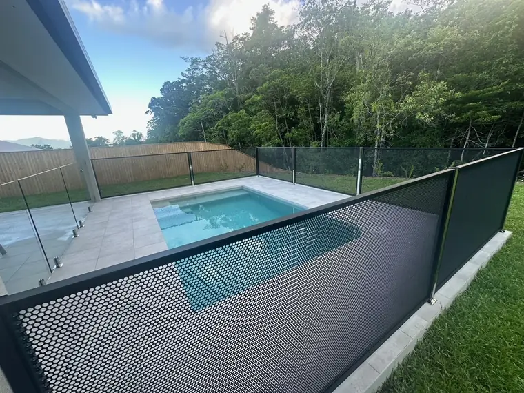 A black PoolPerf panel in the foreground and a glass panel beside it, both around a small backyard pool