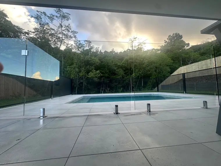 A glass panel on the left and a black PoolPerf fence on the right around a pool at dusk