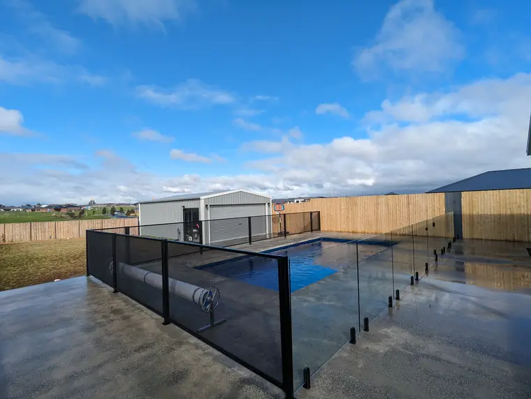 A wet paved pool area after rain with a black PoolPerf fence and a glass panel side by side