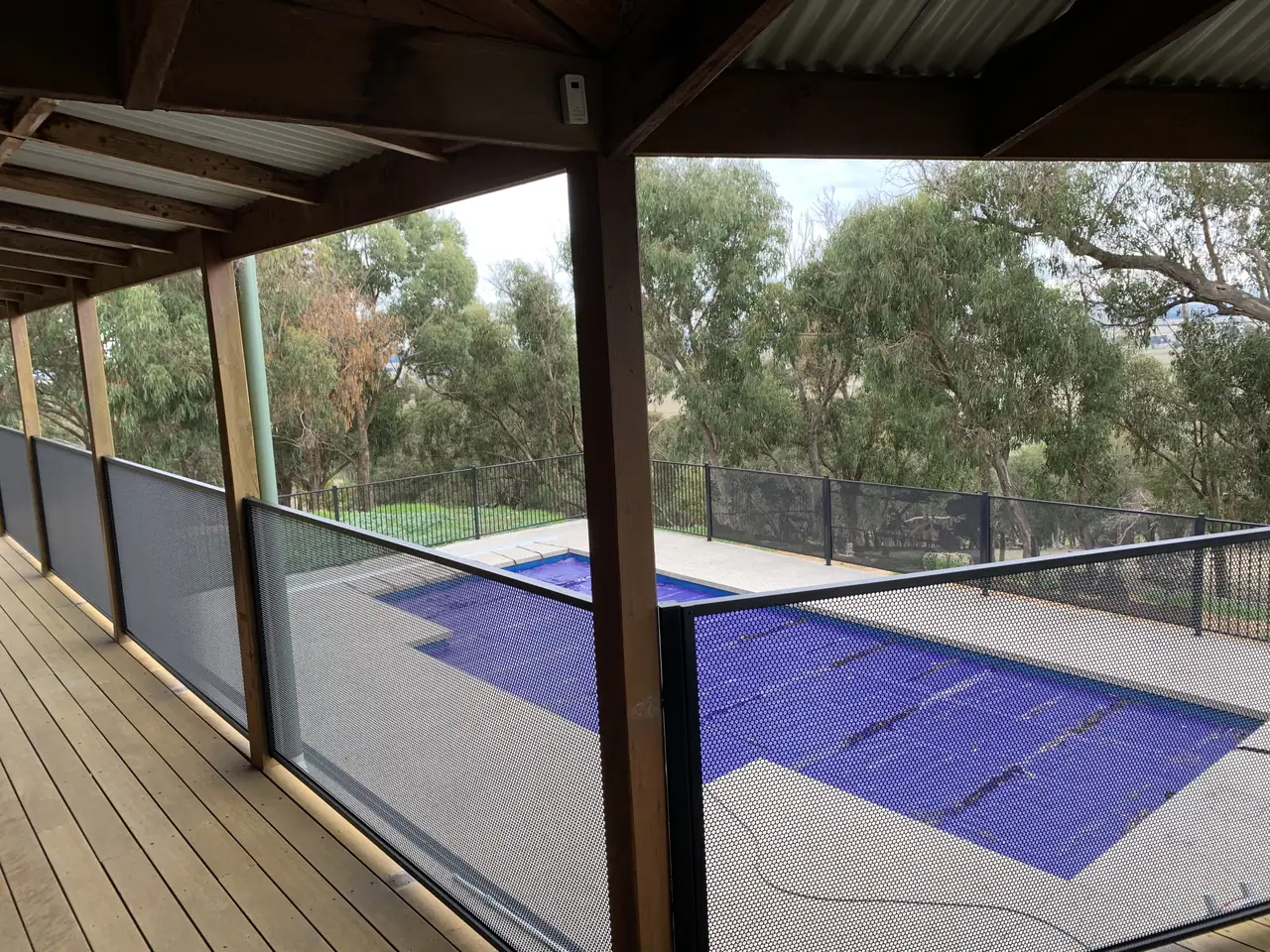 A black perforated balustrade along the edge of a covered timber deck in Victoria, looking down to the pool and its fence