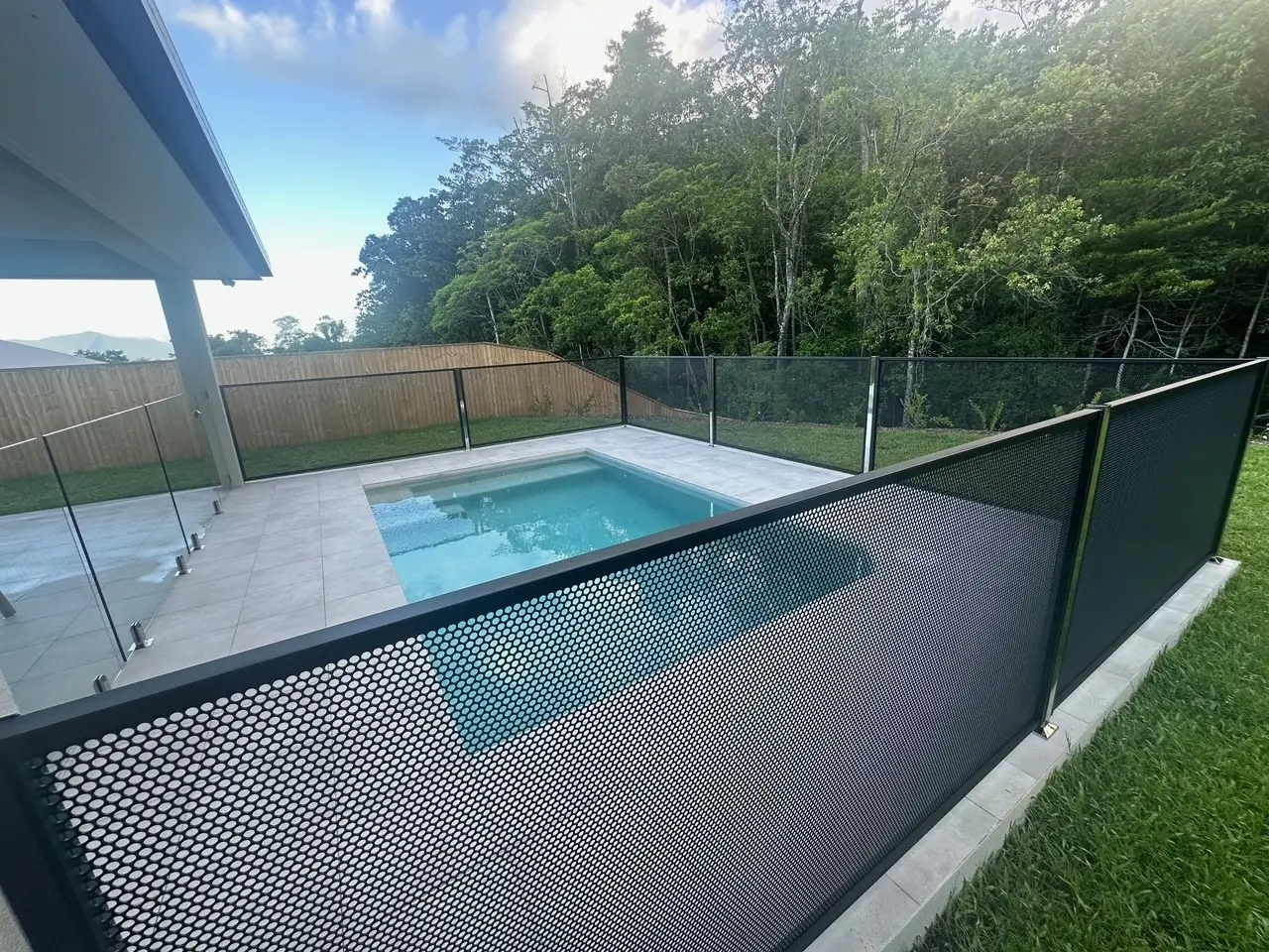 A black PurePerf fence along the lawn side of a Queensland pool, with glass on the house side and rainforest beyond the back fence