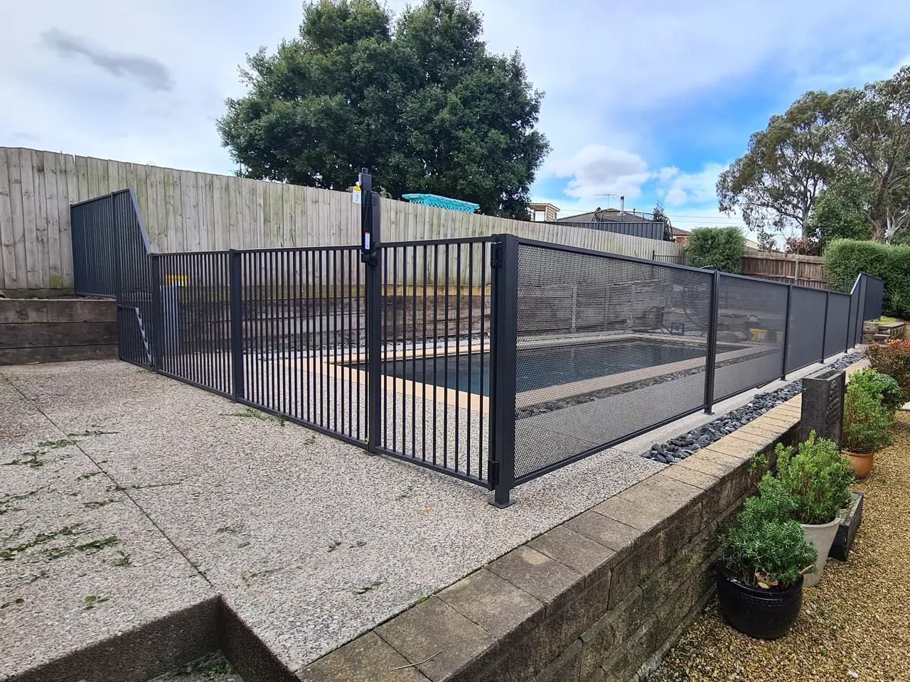 A flat top gate and fence beside a Victorian pool, with black PurePerf panels along the retaining wall behind