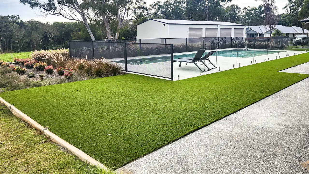 Glass along a new pool on artificial grass in Queensland, with Monument grey PoolPerf along the garden bed behind it