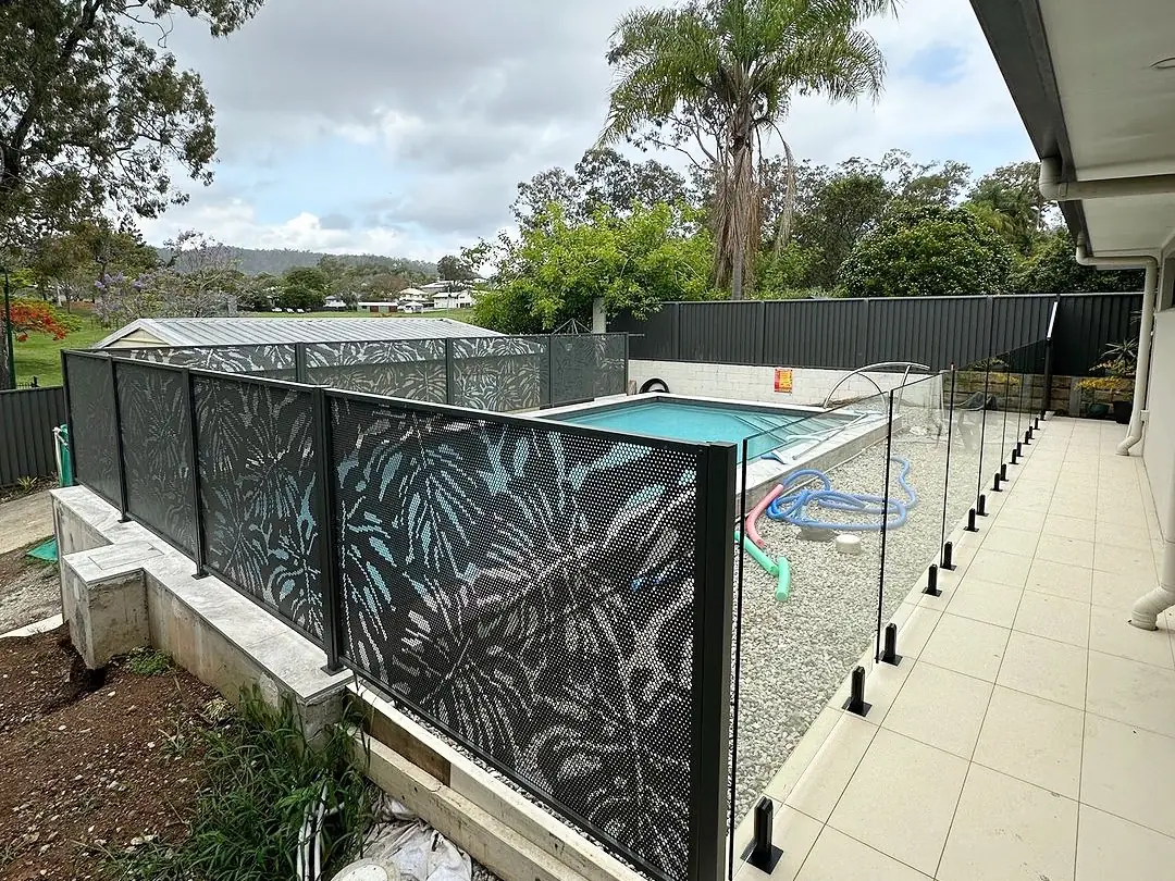 Black Monstera design PoolPerf panels along the garden edge of a Queensland pool, with glass along the tiled walkway beside the house