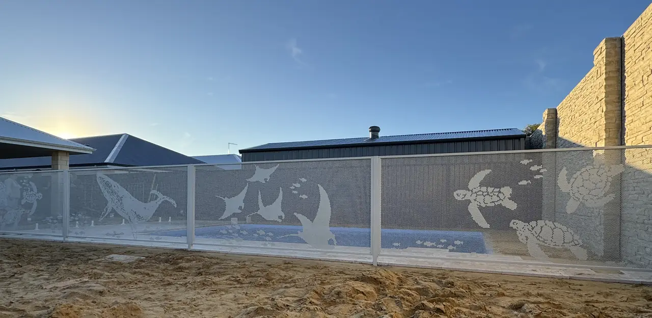 A white custom PoolPerf fence in Western Australia with whales, turtles and manta rays cut into the panels, against a sunrise