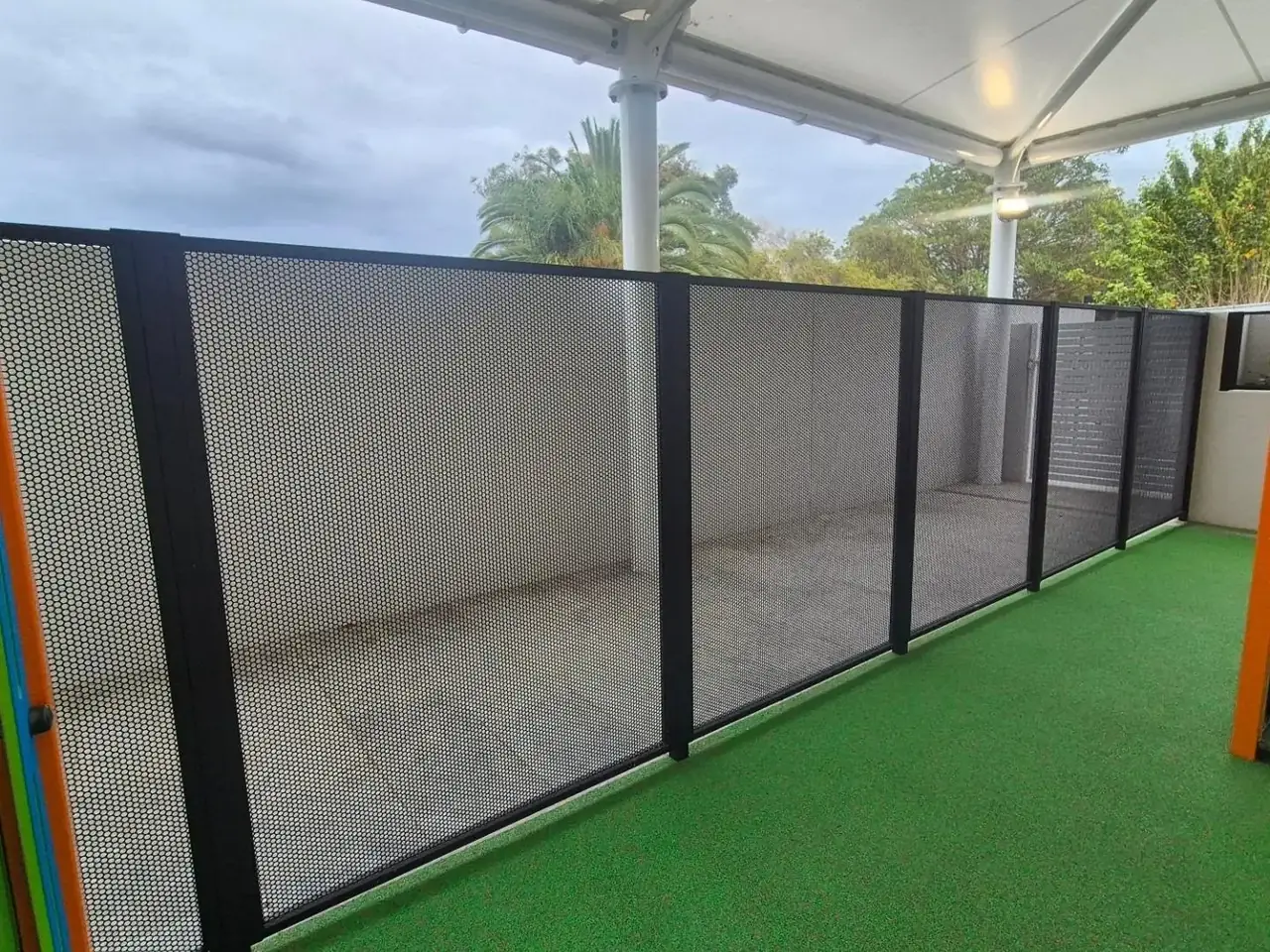 A run of plain grey perforated panels on artificial turf around a play area
