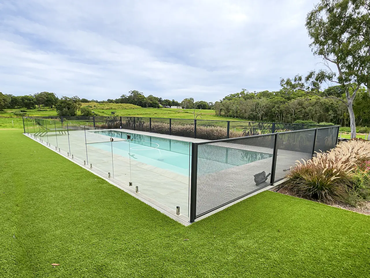 A long pool on a lawn in Queensland with frameless glass along the near side and Monument grey PoolPerf panels along the far side and the end