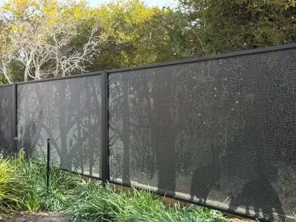 A long black perforated fence with a tree silhouette along a garden boundary