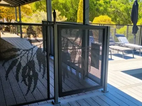 Grey perforated panels between black posts on a deck, with a gum leaf design gate
