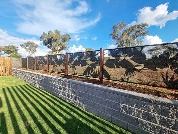 Black custom design panels fixed on top of a block retaining wall, above a striped lawn
