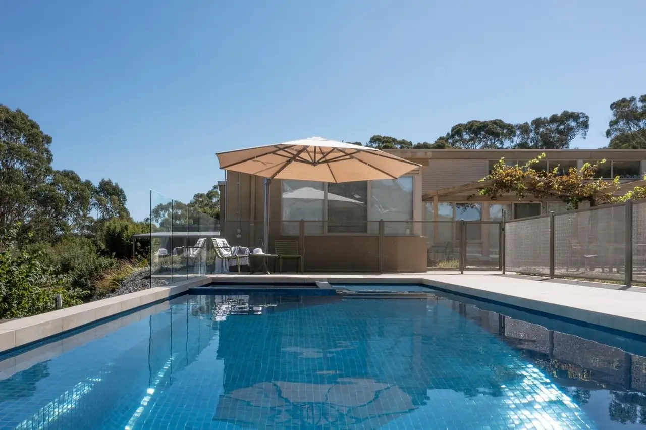 A Victorian pool with an umbrella on the paving, black PurePerf panels along one side and glass along the other