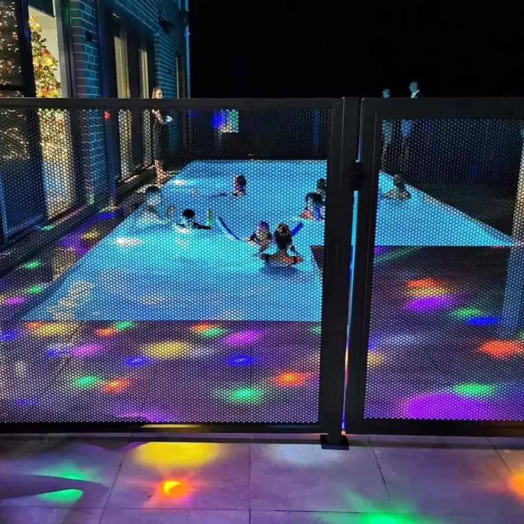 A family night swim with coloured pool lights shining through a PoolPerf fence