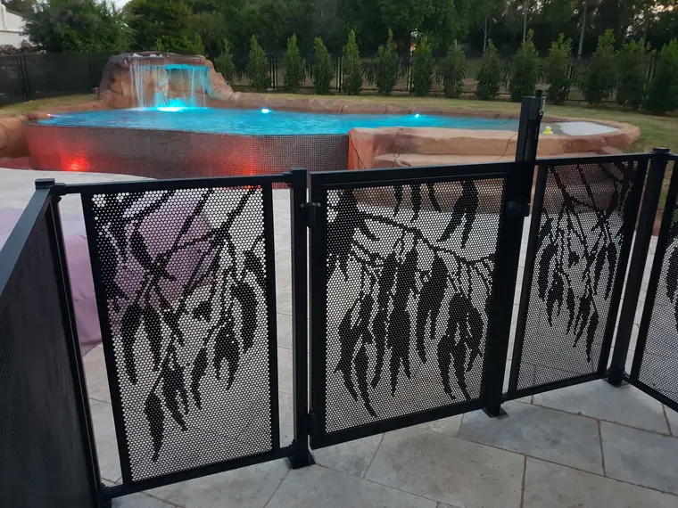 Bracket Fit: black Gum design PoolPerf panels and a gate held to the posts by small brackets, beside a rock pool at dusk
