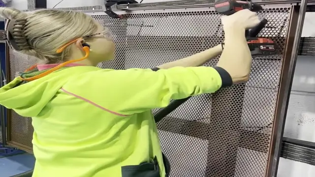 A fabricator in the PoolPerf factory riveting a perforated sheet into its frame
