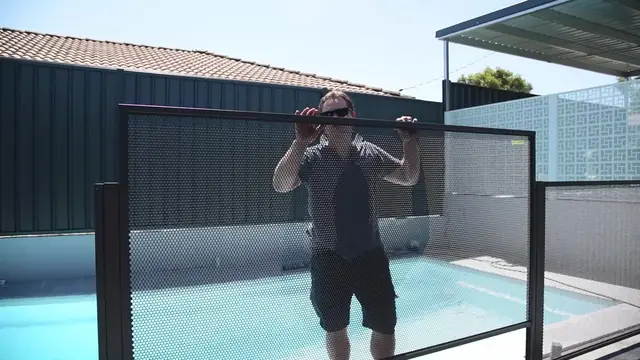 An installer lifting a black PoolPerf panel into place between two posts beside a pool