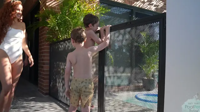 Two young boys reaching up to the latch of a closed PoolPerf gate as their mum walks over