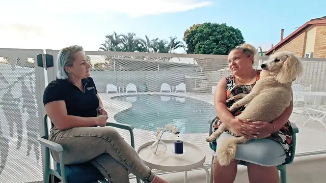 A PoolPerf owner with her dog on her lap, being interviewed beside her pool and her white Gum design fence