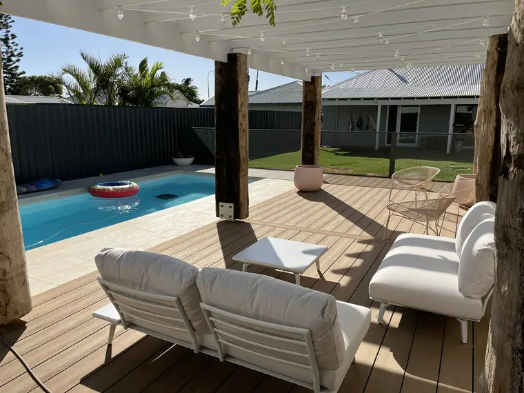 An outdoor lounge on a timber deck in Western Australia looking across a pool to a Woodland Grey PoolPerf fence and the lawn beyond