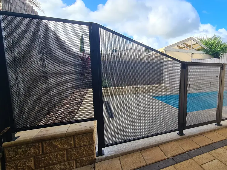 A black PoolPerf fence in South Australia where one panel is cut on an angle, its top edge running down from a tall panel on a retaining wall to the normal fence height
