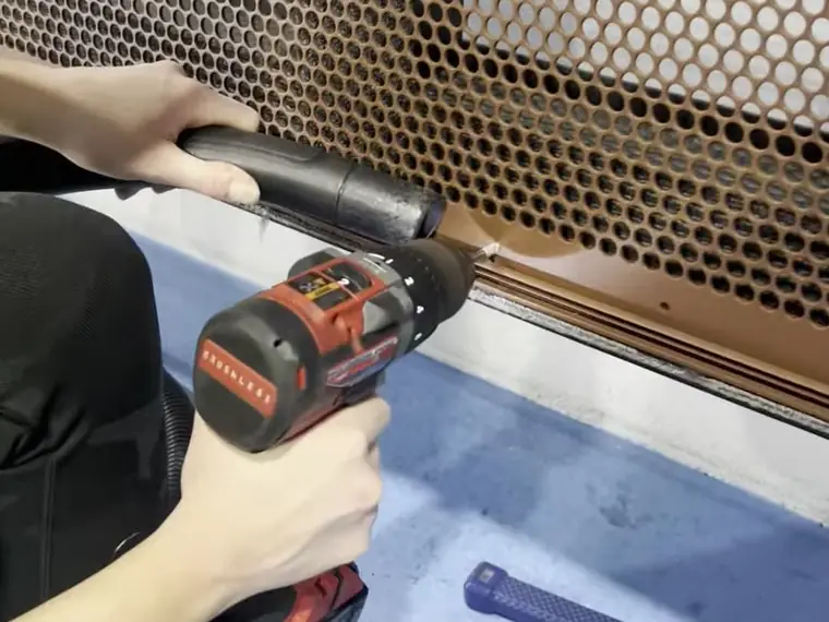 A fabricator in the PoolPerf factory riveting a perforated sheet to the edge of its frame, with a vacuum hose held beside the rivet gun