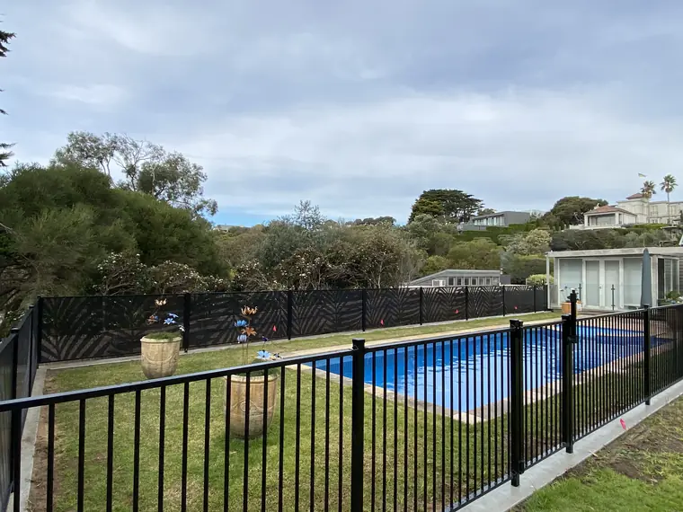 A backyard pool in Victoria with a flat-top fence of upright bars in the foreground and a black Palmy design PoolPerf fence along the back