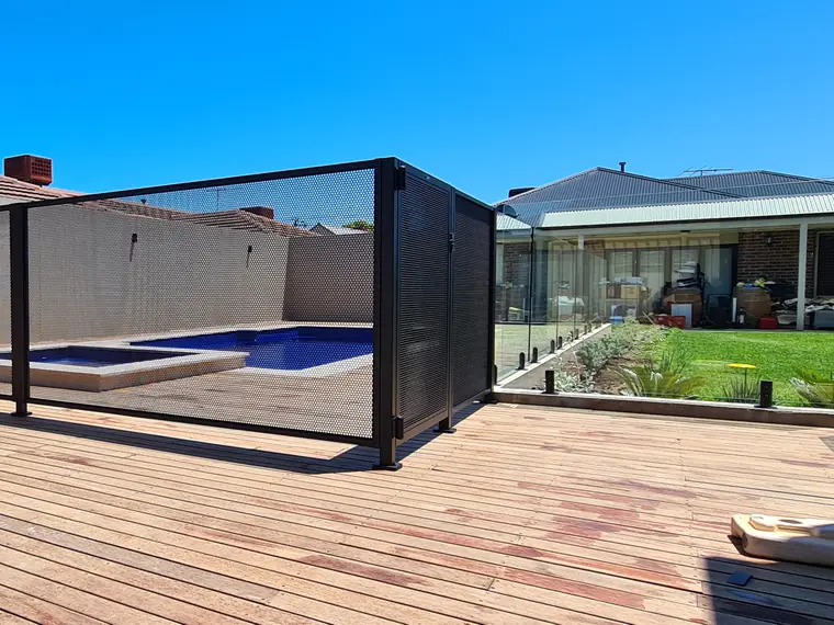A timber deck in South Australia with black PoolPerf panels around a spa and pool, and a run of glass panels beyond them beside the lawn